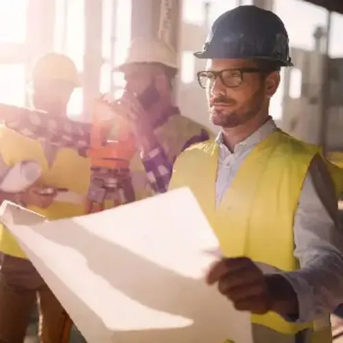 A man in yellow vest holding paper near others.